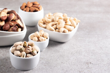 Large assortment of nuts in different bowls on stone table.