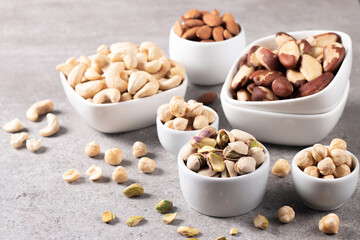 Large assortment of nuts in different bowls on stone table.