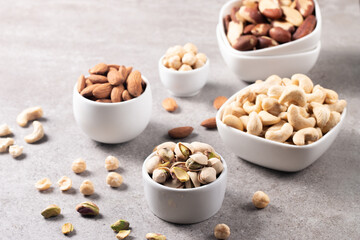 Large assortment of nuts in different bowls on stone table.