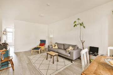 a living room with white walls and wood flooring in the center of the room, there is a grey couch