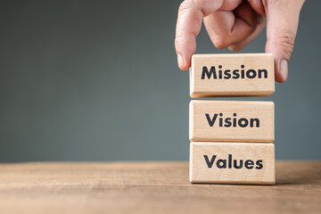 Hand arranges the wood blocks into stack with text, Mission, Vision, Values, brand loyalty,...