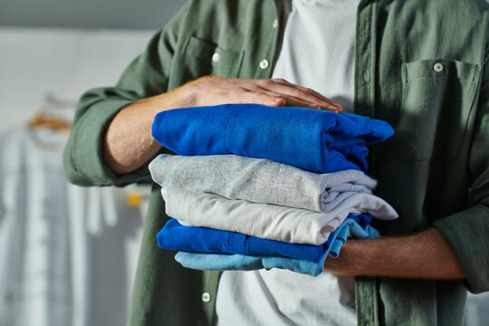 Cropped view of young craftsman in casual clothes holding clothing while standing and working in blurred print studio, customer-focused entrepreneur concept