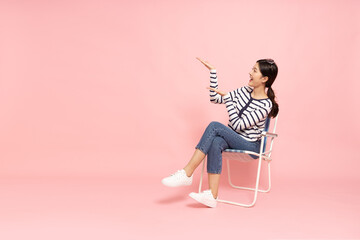 Young Asian woman sitting and presenting to empty copy space isolated on pink background
