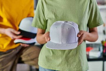 Cropped view of young african american designer holding snapback while standing near blurred...