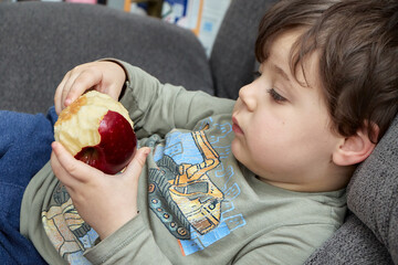 cute young boy eating an apple on the couch