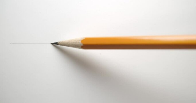 Drawing a straight line across paper with a yellow pencil.