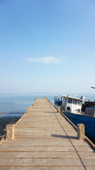 Fototapeta premium A wooden bridge Harbor with boats anchored on the island of East Nusa Tenggara. wooden pier bridge with sea and beautiful blue sky. Vertical view. Sea background