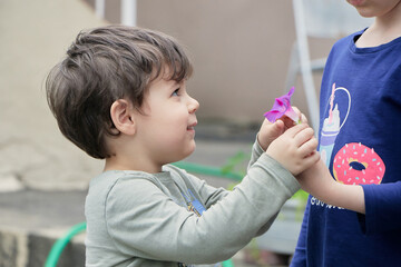 brother and sister playing with a purple flower in the backyard