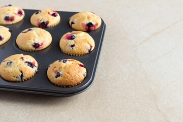 Homemade tasty berries cupcakes with black currant or blueberry in a black metal non-stick cake mold on a beige stone background. Summer baking.