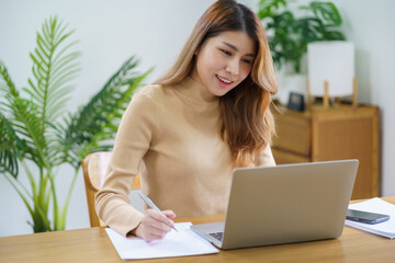 Happy beautiful Asian woman using computer laptop for work online at living room.