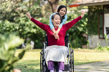 Asian senior woman in wheelchair with happy daughter. Family relationship retired woman sitting on wheelchair in the park age care at retirement home.