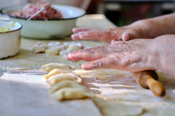 Rolling out dough with rolling pin and hands for cooking dumplings.