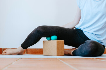 Woman doing self myofascial release of hamstrings with two massage balls on cork block