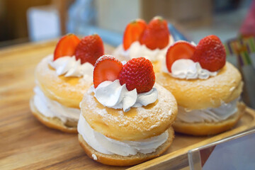 Strawberry cream donuts are sweet and crunchy, soft texture filled with cream topping with fresh, colorful stories. Appetizing placed in trays on the shelf in the coffee shop for sale to customers.   