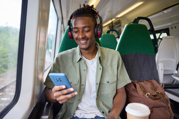 Young Man Commuting To Work On Train Sitting  On Train Looking At Mobile Phone For Travel...