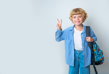 Primary school smiling boy girl with backpack showing victory peace sign smiling at camera. Copy space for advertising blank concept. Back to school. Childhood, education, products for children