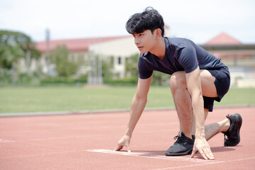 Fototapeta premium An asian man ready to run at start point with concentration emotion at sport field background.