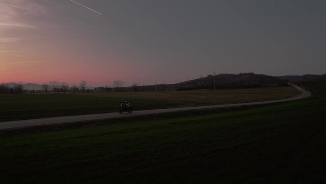 Aerial view of a motorcyclist riding along a road in the fields crossing the hills in the Monferrato wine region.