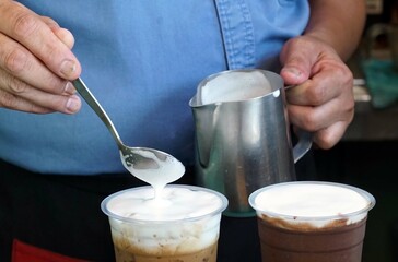 Barista pouring milk into a cup of ice coffee in coffee shop, for creative design coffee cafe.