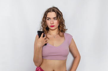 Obraz premium Brunette is holding a phone. Sexy woman in a lilac short top. Bright makeup.