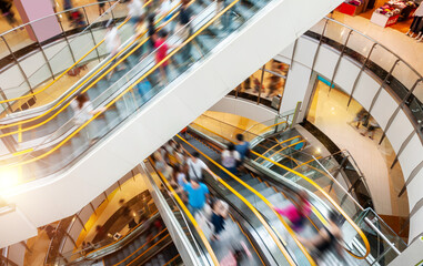 People on many fast moving escalators in modern shopping mall
