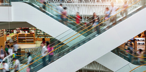 People on many fast moving escalators in modern shopping mall