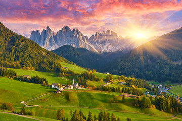 Amazing autumn scenery in Santa Maddalena village with church, colorful trees and meadows under rising sun rays. Dolomite Alps, Italy. - 624890627