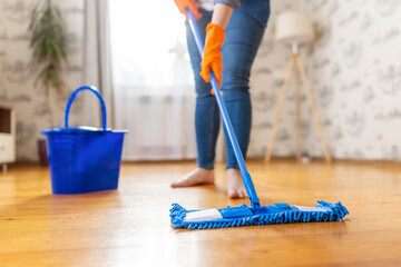 Woman in casual clothes washing a wooden floor with a damp microfiber mop