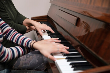Two girls having fun together - playing the classical four-handed piano, teaching each other the nuances of playing the piano, music concept