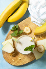 Banana smoothie with melon in drinking glass on wooden board on a stone background. Detox menu. Fresh seasonal smoothies. View from above.