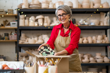 Woman seller or worker of earthenware shop packing order of client and wrapping it into paper.