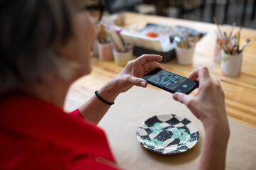 Pottery master woman photographing work result, using mobile phone for taking picture of earthenware
