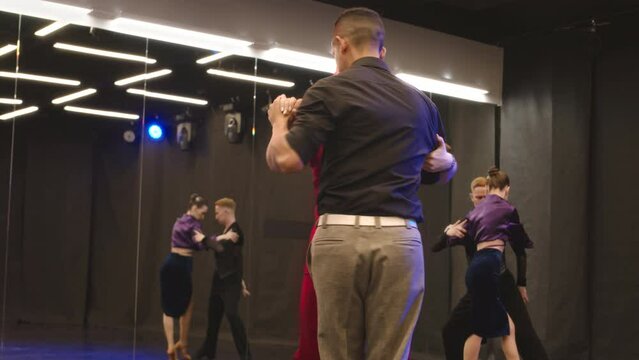 Medium slowmo of diverse couple of dancers dancing dynamic and sensual bachata in spacious mirrored dance studio