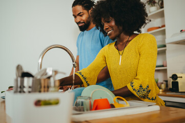 A cheerful african american couple is doing dishes and cooking lunch at home together.