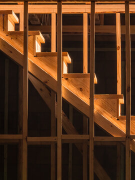 Side view of a new wooden staircase, with wall studs on either side, illuminated by afternoon sunlight in a single-family suburban house under construction in southwest Florida