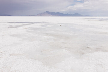 Fototapeta na wymiar A beautiful unusual landscape on which a large desert of white salt and blue mountains in the distance on cloudy day. Bonneville Salt Flats, Utah, USA - 19 June 2023