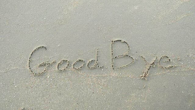 Message GoodBye  written on beach sand background. 
Word Good bye lapping waves happy New Year coming concept.