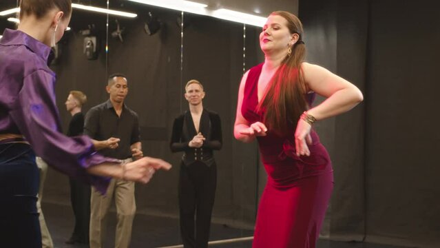 Medium Shot Of Two Young Diverse Women In Fancy Outfits Latina Dancing In Ballroom While Their Male Partners Watching And Clapping