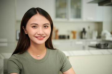 Portrait of cheerful young Asian woman in t-shirt standing in kitchen