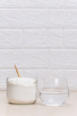Glass of water and a jar of collagen goodnesson a marble beige background.