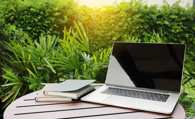 Wood table office outdoors with a tablet and notebook   on green garden background