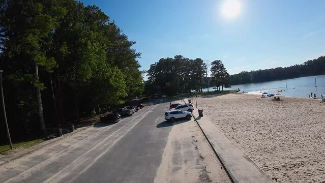 aerial FPV footage of a gorgeous summer landscape at Proctor Landing park with a lake a sandy beach, lush green trees and grass with blue sky and clouds at Lake Acworth in Acworth Georgia USA