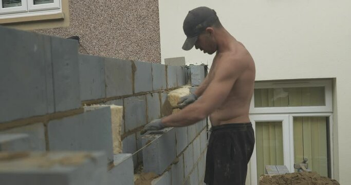Man shirtless bricklaying on a building site mid shot 