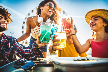 Fototapeta premium Multiracial happy friends toasting cocktail glasses outdoors at summer vacation - Smiling young people drinking alcohol together sitting at bar table - Beverage life style concept