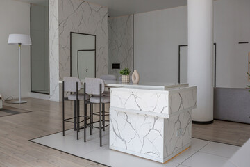 kitchen and dining island with high bar stools in a minimalistic modern luxury design of an expensive house on a sunny day. white walls with plaster, parquet, decorative lighting and no one inside