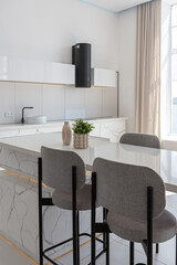 kitchen and dining island with high bar stools in a minimalistic modern luxury design of an expensive house on a sunny day. white walls with plaster, parquet, decorative lighting and no one inside