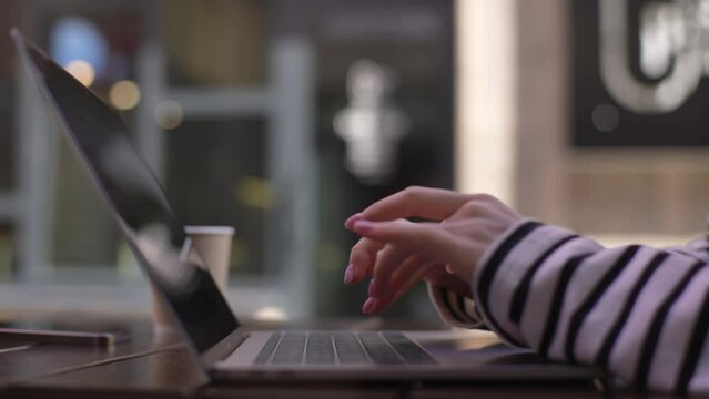 Closeup side view of unrecognizable businesswoman sitting at table in outdoor cafe terrace in summer day, closing lid of laptop when finishing work. Cropped shot of female hand turns off computer.