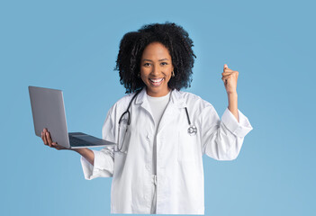 Satisfied young black lady doctor therapist in white coat hold laptop, making success hand gesture