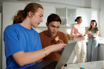 Computer science student showing classmate programming code on laptop screen