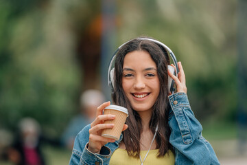 girl outdoors with headphones and cup of coffee